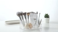 Professional makeup brush set with beauty blender and tools in clear acrylic organizer on white background for cosmetic storage and vanity organization.