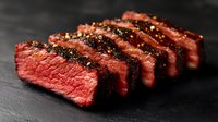 Juicy medium rare beef steak sliced on black stone background, seasoned with black pepper and spices, showing pink center and grilled crust texture.