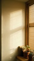 Sunlight streaming through wooden blinds casts linear shadows on a cream wall, creating warm geometric patterns. Potted plants sit on a wooden shelf below the window, bathed in natural light. Use for interior design, home decor, and lifestyle content.