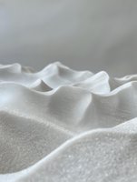Soft white waves of fabric or material creating gentle undulating curves and peaks with delicate texture and shadows in minimalist macro photography style.
