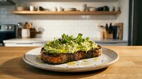 Avocado toast with microgreens on sourdough bread served on ceramic plate in modern kitchen setting. Healthy breakfast or brunch meal concept.