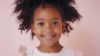 Young African American girl with natural curly hair wearing white lace dress, showing bright genuine smile against pink background, expressing joy and innocence.