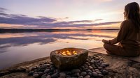 Woman meditating by ocean at sunset with fire bowl on beach. Peaceful spiritual practice during golden hour with calm waves and purple sky reflections.