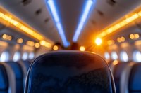 Airplane cabin interior with dramatic lighting showing leather headrest, blue and orange ceiling lights creating atmospheric bokeh effect. Perfect for travel themes.