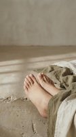 Bare feet relaxing on sandy beach with linen fabric in warm natural sunlight creating peaceful vacation atmosphere for wellness and self-care concepts.
