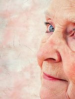 Close-up partial face portrait of senior Asian woman with blue eyes showing gentle smile and wisdom wrinkles against textured pink background.