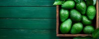 Fresh ripe green avocados in wooden box on dark green wooden background, top view with copy space. Natural organic food concept.