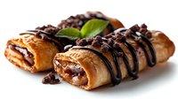 Flaky pastry rolls filled with chocolate and nuts, drizzled with dark chocolate sauce and garnished with fresh mint leaf on white background.