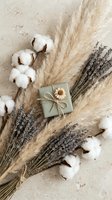 Natural spa composition with dried lavender, cotton flowers, pampas grass and wrapped gift on neutral textured background for wellness branding.