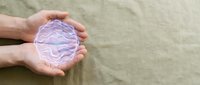 Hands gently holding glowing purple brain illustration on textured beige background representing mental health awareness, neurology care and cognitive wellness.