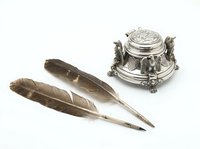 Vintage silver inkwell with ornate handles and two natural feather quills isolated on white background, ready for antique design, historical illustrations, and classic stationery projects.