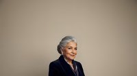 Senior woman with gray hair wearing black blazer against neutral beige background, suitable for corporate, business, and professional lifestyle content.