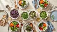 Fresh healthy salad bowls with mixed greens, vegetables and colorful toppings arranged on wooden table for nutritious meal planning and clean eating lifestyle.