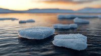 Floating ice chunks on dark rippling water at sunset, dramatic orange sky reflection creates serene winter atmosphere, close-up nature photography.