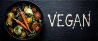 Fresh vegan salad with roasted carrots, cherry tomatoes, and greens in a dark bowl on slate, with the word vegan written in sauce.