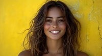 Young Hispanic woman with natural wavy brown hair and bright authentic smile against vibrant yellow wall background, radiating joy and confidence in summer portrait.