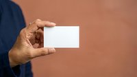 Close-up of male hand holding blank white business card against warm brown background, suitable for corporate branding and identity mockups.