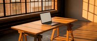 Modern wooden desk with laptop in sunlit office space featuring geometric window shadows and warm natural lighting for remote work productivity.