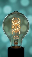 Vintage Edison light bulb with glowing spiral filament against turquoise bokeh background for creative lighting and interior design concepts.