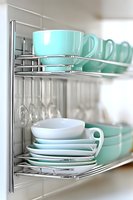 Modern kitchen organization with mint green ceramic dishes and cups neatly arranged on chrome wire shelving rack for efficient storage and display.
