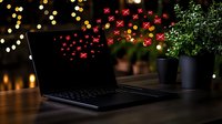 Laptop on dark wooden table with festive bokeh lights and decorative red hearts floating, romantic home office setup with potted plants at night.