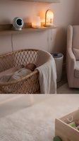 Cozy modern nursery with sleeping newborn baby in wicker bassinet, baby monitor and warm ambient lighting creating peaceful bedtime atmosphere.