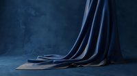 Elegant navy blue silk fabric draped on textured floor against moody blue backdrop, showcasing luxurious material for fashion, interior design, and product photography projects.