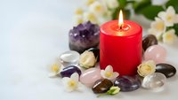 Red candle burning surrounded by healing crystals amethyst rose quartz jasmine flowers spa wellness meditation relaxation aromatherapy holistic therapy.