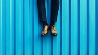 Business professional legs in dark suit and brown leather shoes against vibrant blue striped wall for corporate and fashion concepts.