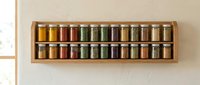Wooden wall-mounted spice rack displaying colorful glass jars with various dried herbs, spices and seasonings organized in two rows for kitchen storage and organization.