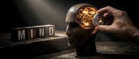 Silhouette of male head with glowing lightbulb inside brain, hand inserting golden bulb, wooden blocks spelling mind on dark surface, conceptual composition for innovation and creativity themes.