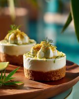 Mini cheesecakes with deviled egg topping garnished with fresh dill and spices on wooden serving platter, perfect for gourmet appetizers.