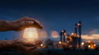 Hands holding glowing solar panel with industrial plant and bokeh lights at dusk, representing renewable energy, sustainability, and green power technology for business concepts.