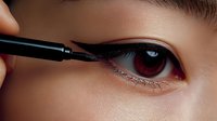 Close-up of woman applying black eyeliner pencil to lower lash line. Professional makeup application technique for eye enhancement and beauty routine.