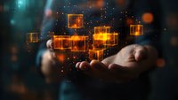 Glowing orange cubes floating above hands against dark background with bokeh effect, representing digital transformation and blockchain technology concept.