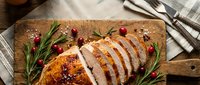 Sliced roasted chicken breast with fresh rosemary and cranberries on wooden cutting board, ideal for food styling, culinary blogs, and restaurant menus.