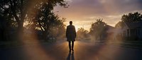 Silhouette of person walking down empty suburban street at golden hour sunset with dramatic sky and residential homes creating peaceful neighborhood scene.