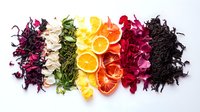 Colorful dried flowers, tea leaves and citrus fruit slices arranged in rainbow spectrum on white background, overhead view of natural organic ingredients for herbal tea blend.