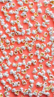 Fresh popcorn scattered on coral pink background, creating playful pattern. Movie snack food photography with white fluffy kernels in flat lay composition.
