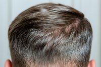 Close-up view of short brown hair styled in modern male haircut showing texture and layering details against light background, demonstrating professional hairstyling technique.