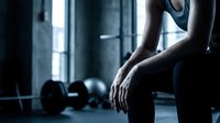 Young athletic woman resting after intense workout in modern gym, sitting with dumbbells nearby, fitness and recovery concept for health and wellness.