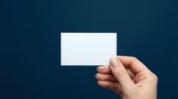 Hand holding blank white business card against dark navy blue background, mockup template with copy space for branding design.
