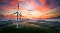 Wind turbines generating renewable energy on rolling hills at dramatic sunset with orange and pink sky clouds creating sustainable power landscape.