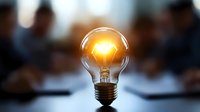 Glowing light bulb with warm yellow illumination against blurred business meeting background symbolizes innovation, creativity and bright ideas.