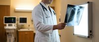 Male doctor examining chest x-ray film on lightbox in modern hospital room. Medical professional analyzing lung radiograph for diagnosis and treatment.