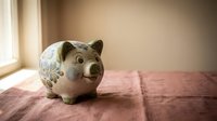Ceramic piggy bank with floral pattern sitting on pink fabric surface near window with soft natural lighting for savings and financial planning.