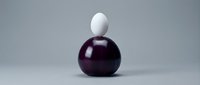 White egg balanced on dark purple sphere against gray background showcasing equilibrium and contrast in minimalist composition for design projects.