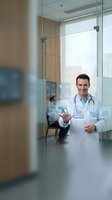 Smiling male doctor with stethoscope presenting digital healthcare technology icons in modern medical office with glass walls and contemporary design.