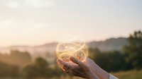 Hands holding glowing orb of light energy against sunset landscape background symbolizing hope, spirituality, and inner power for wellness concepts.