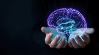 Glowing holographic brain floating above open hands on dark background representing artificial intelligence, neuroscience and mental health concepts.
